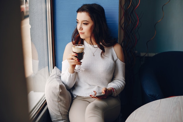 Free photo girl in a white sweater sitting alone in cafe