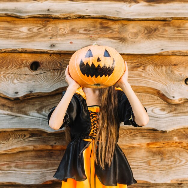 Girl in witch costume closing face by pumpkin