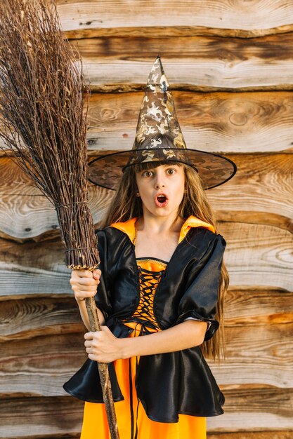 Girl in witch costume making face with broomstick