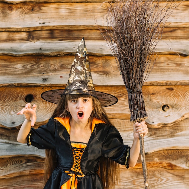 Девушка в костюме ведьмы, показывающая ужас с метлой