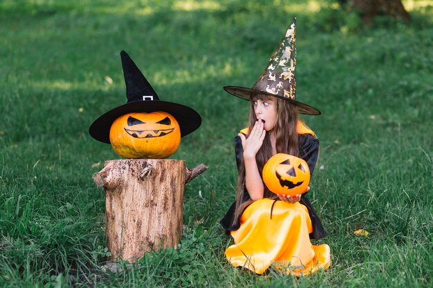 Girl in witch costume showing surprise near pumpkin