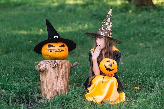 Girl in witch costume showing surprise near pumpkin