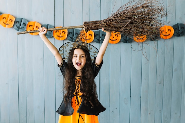 Girl in witch suit holding broom in raised hands