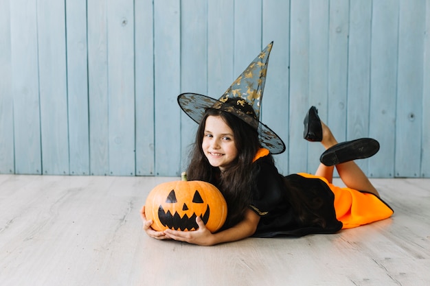 Girl in witch suit lying on floor with pumpkin