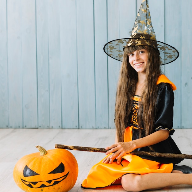 Foto gratuita ragazza in costume da strega e cappello a punta seduto sul pavimento e sorridente