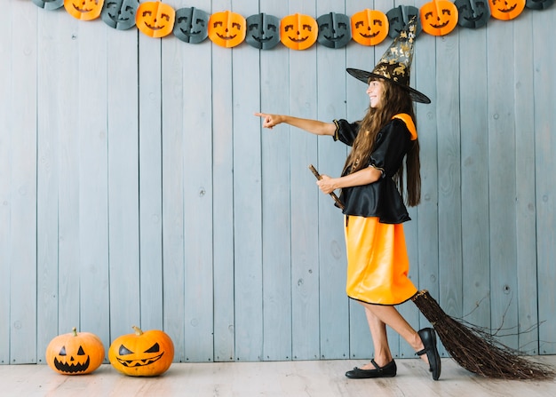 Girl in witch suit standing with broom pointing away