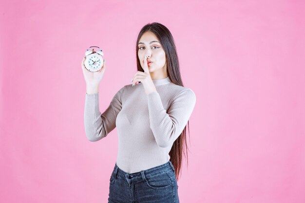 Girl with an alarm clock makes silence sign