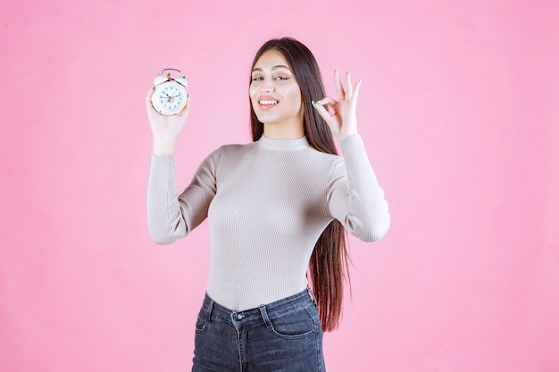 Girl with an alarm clock making enjoyment sign