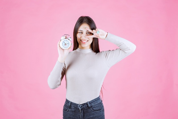 Girl with an alarm clock making peace sign