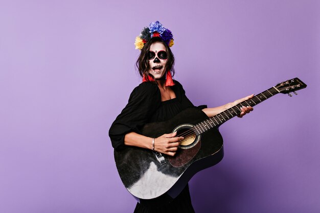 Girl with art on her face sings serenade and plays guitar.