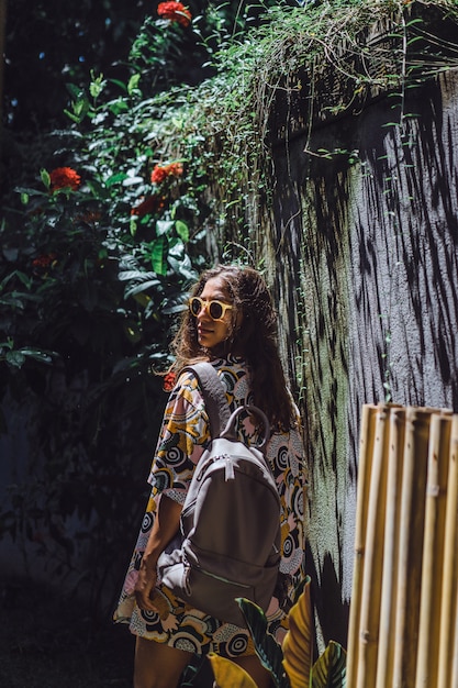 girl with a backpack, wearing sunglasses, in a tropical garden