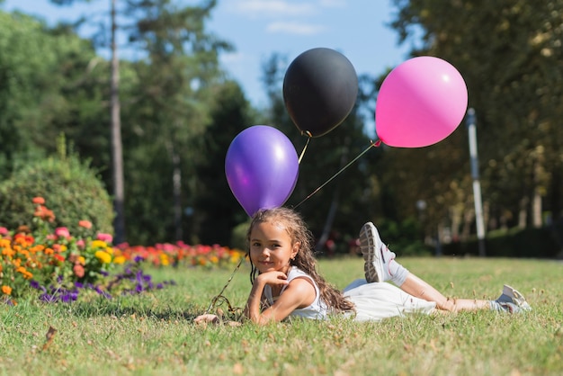 Girl with balloons lying in grass