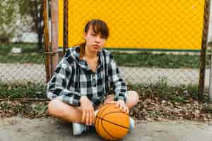 Free photo girl with basketball sitting in front of fence