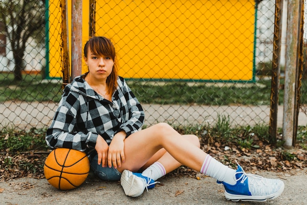 Girl with basketball sitting in front of fence