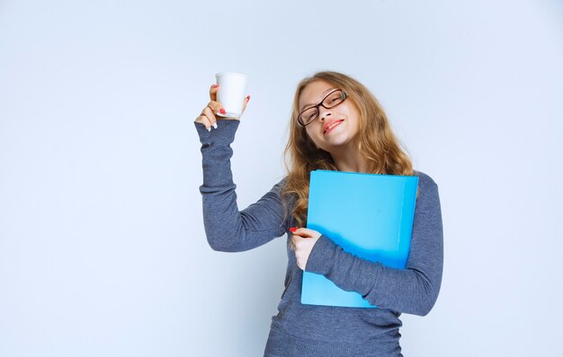 使い捨てのコーヒーカップを保持している青いフォルダーを持つ少女。