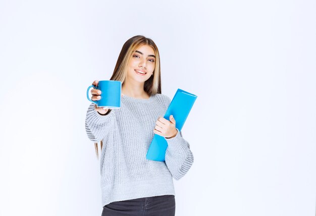 Girl with a blue folder sharing a cup of coffee with her colleague.