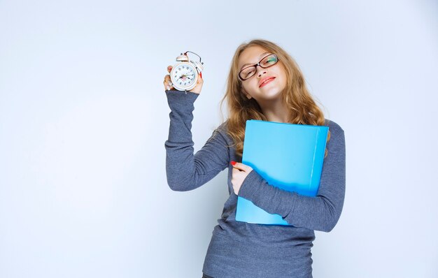 Girl with a blue folder showing her alarm clock.