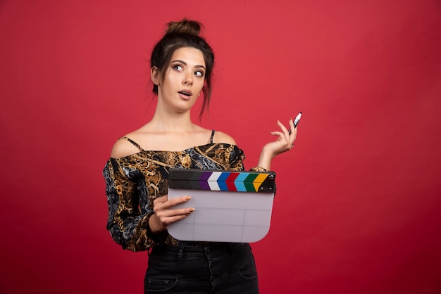 Girl with a clapper board looks thoughtful and confused. 