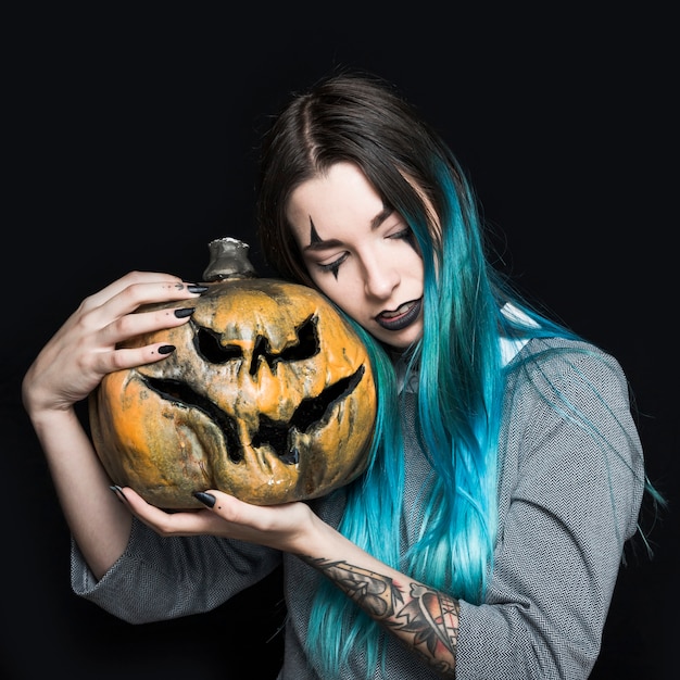 Girl with clown makeup holding creepy pumpkin