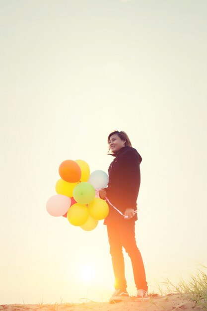 Girl with coloful balloons in sunset