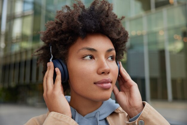 girl with curly Afro hair enjoys new audio song in wireless headphones listens record audio likes audio web content dressed casually poses