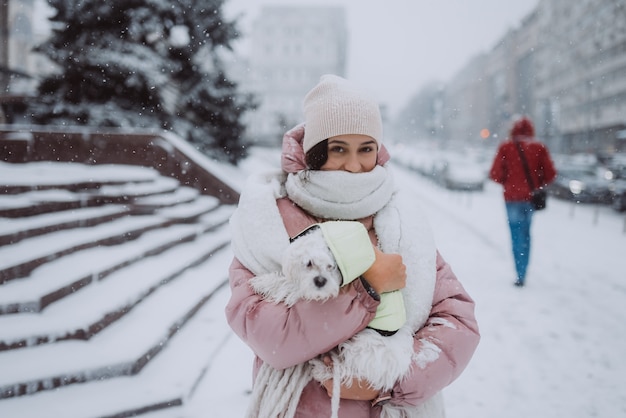 Girl with a dog in her arms on a city street snow is falling