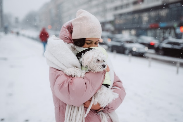 Girl with a dog in her arms on a city street snow is falling