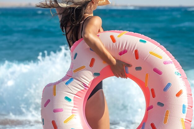 Девушка с кругом в форме пончика на берегу моря. Концепция отдыха и развлечений на отдыхе.