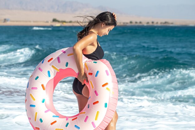 海沿いにドーナツ型の水泳サークルを持つ少女。休暇中のレジャーとエンターテイメントの概念。