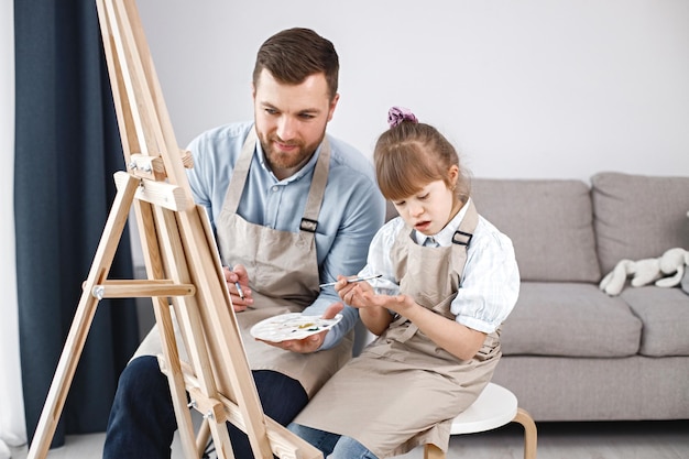 ダウン症の少女と彼女の父親がブラシでイーゼルに絵を描く