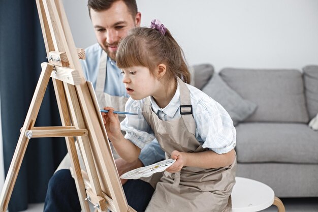 ダウン症の少女と彼女の父親がブラシでイーゼルに絵を描く