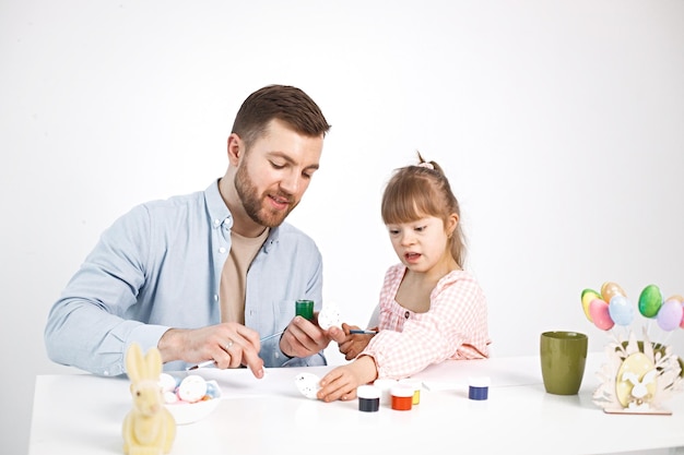 다운 증후군을 앓고 있는 소녀와 그녀의 아버지는 부활절 달걀을 칠하고 있습니다.