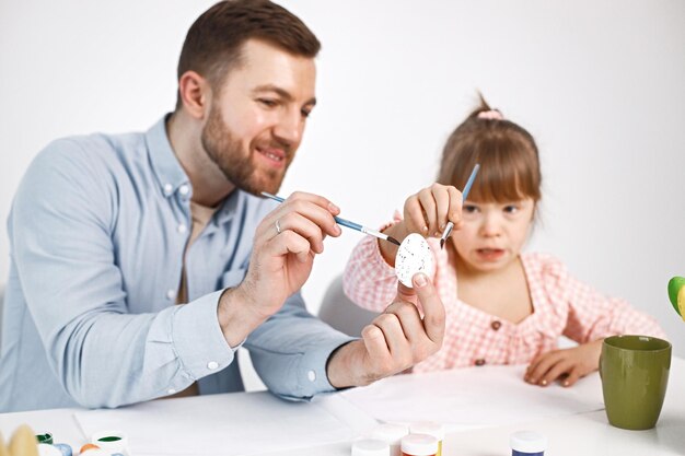 Girl with Down syndrome and her father painting Easter colored eggs