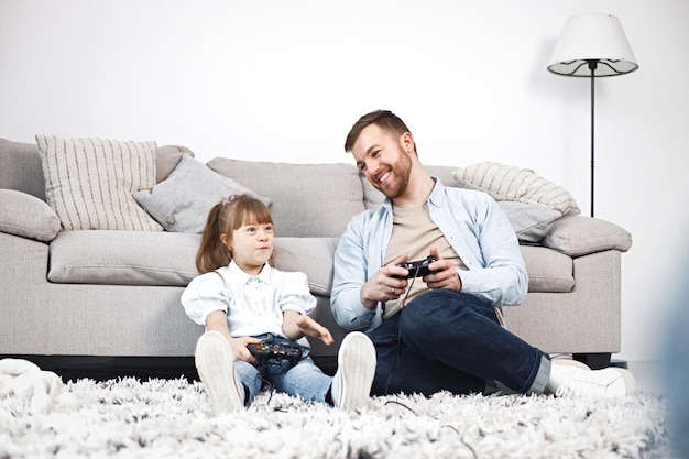 ダウン症の少女と彼女の父親が床に座ってプレイステーションをプレイ