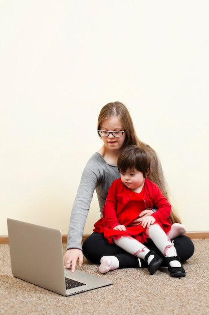 Girl with down syndrome holding child while looking at laptop