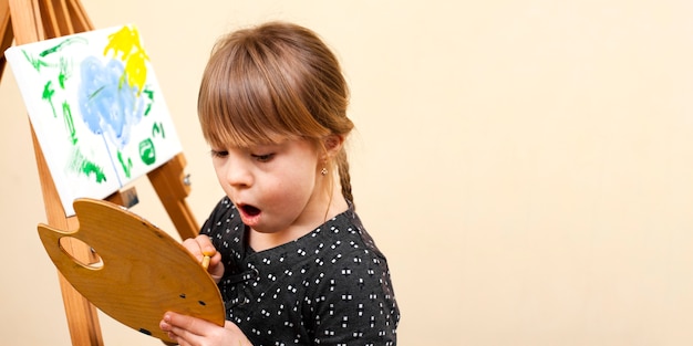 Free photo girl with down syndrome holding palette and painting