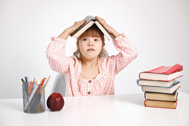 Girl with Down syndrome sitting at desk and holding a book on her head