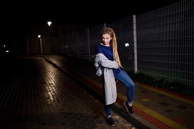 Girl with dreadlocks walking at night street of city