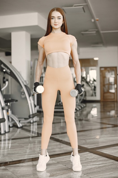 Girl with ginger hair holding two dumbbells. She is at the gym, going to exrcise.