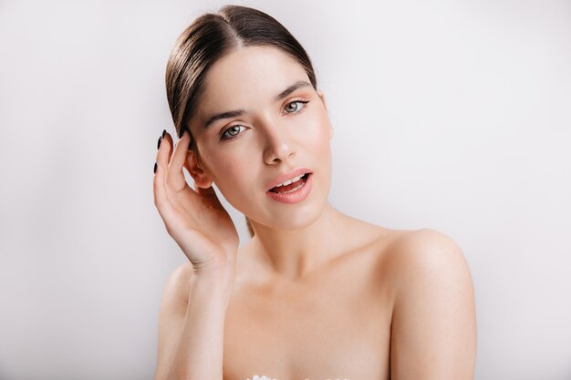 Girl with green eyes and dark hair. Portrait of model with healthy skin on white wall.