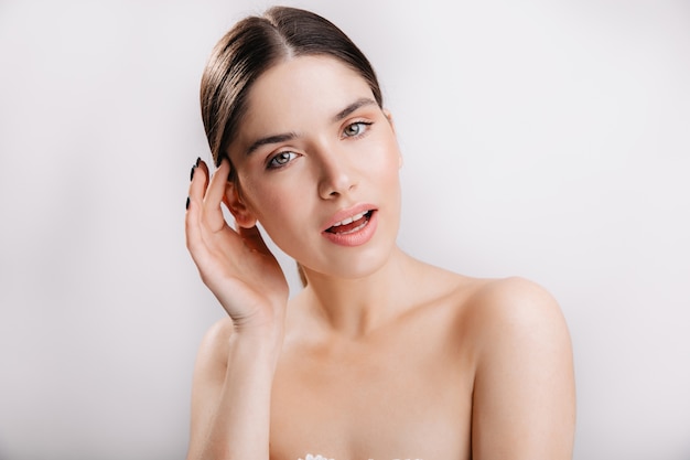 Girl with green eyes and dark hair. Portrait of model with healthy skin on white wall.