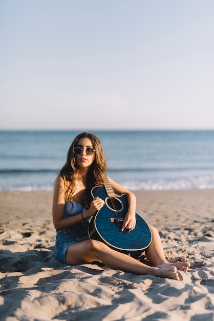 Girl with guitar sitting on the sand