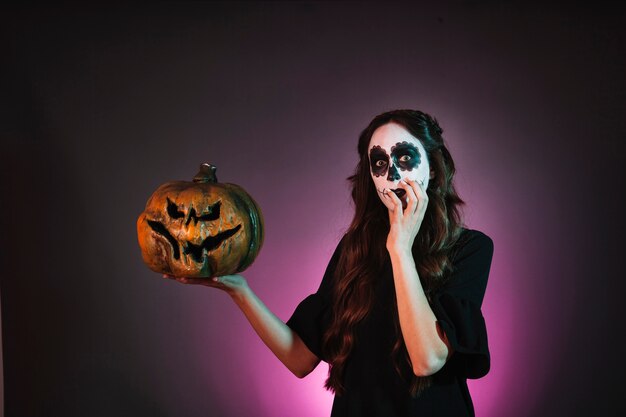 Girl with halloween makeup holding pumpkin