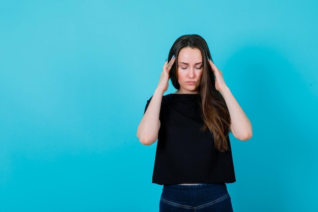 Girl with headache is holding hands on temples on blue background