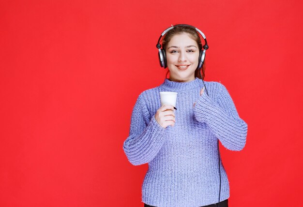 Girl with headphones holding a coffee cup and showing enjoyment sign. 