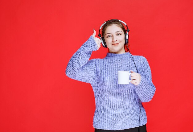 コーヒー マグを持ち、笑顔のヘッドフォンを持つ少女。