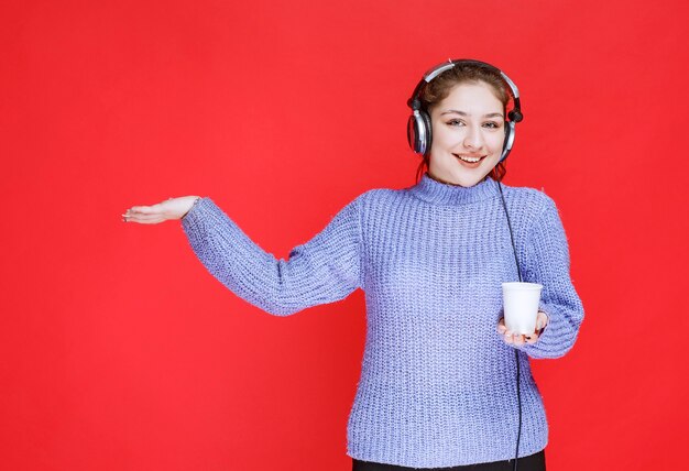 Girl with headphones holding a disposable cup of coffee. 