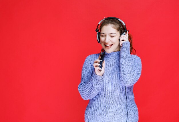 Girl with headphones setting music at her smartphone and enjoying it. 