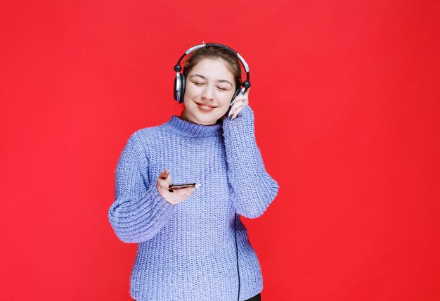 Girl with headphones setting music at her smartphone and enjoying it. 