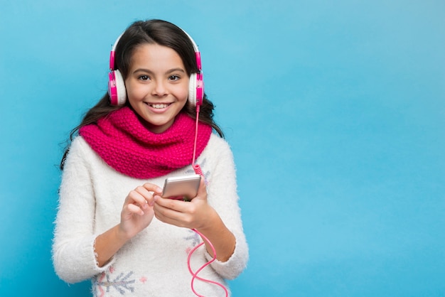 Ragazza con le cuffie e lo smartphone su fondo blu